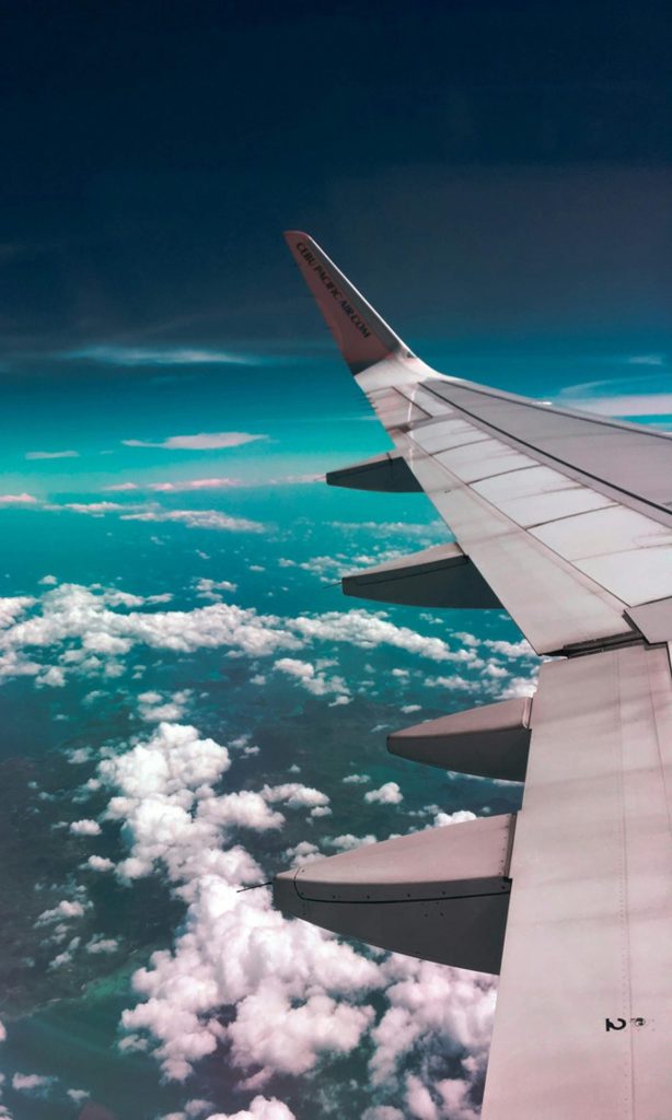 Aerial view of airplane wing over fluffy clouds with a deep turquoise sky.